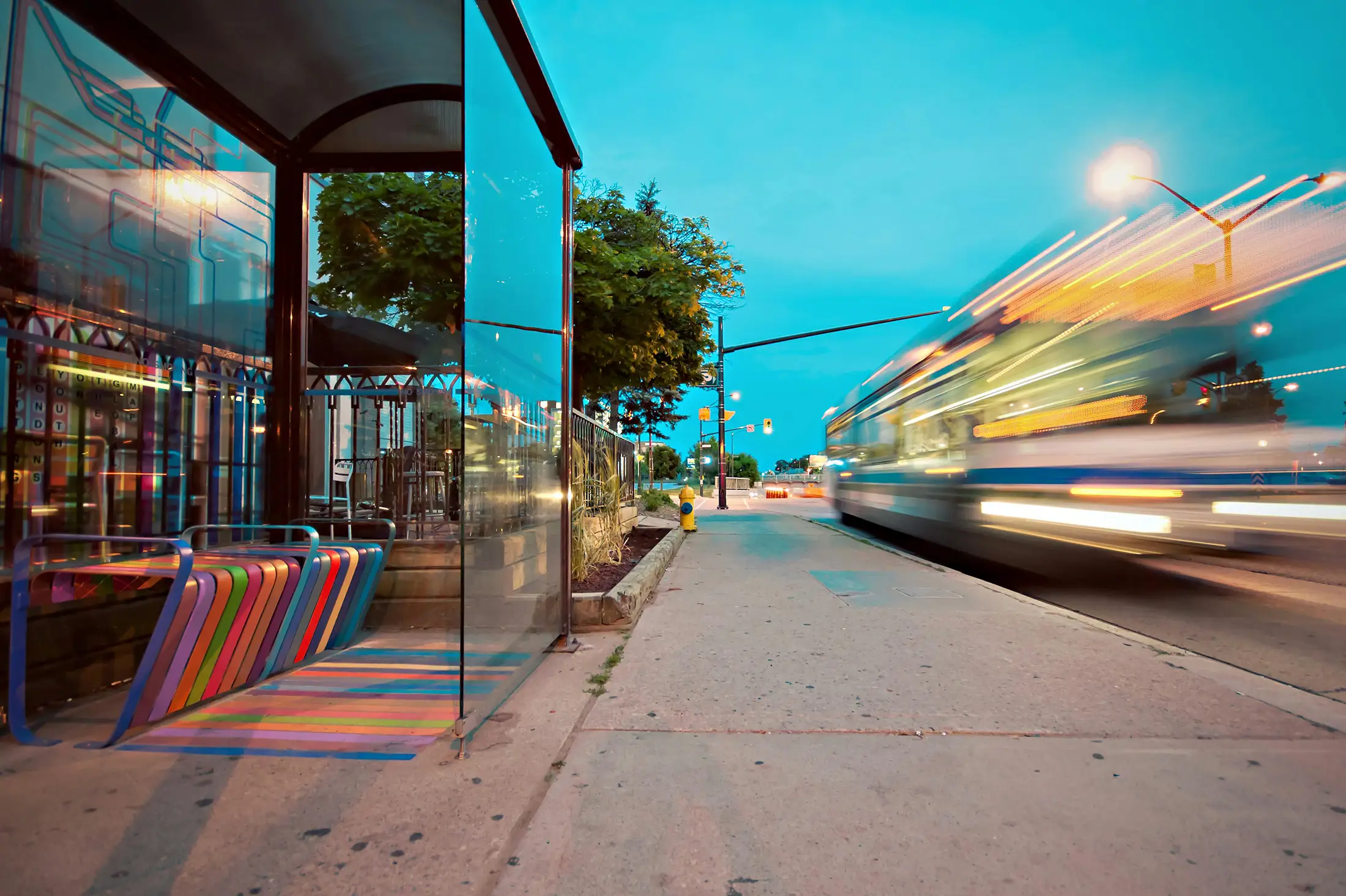 Blurred city bus passing a modern glass bus stop at dusk, symbolizing urban mobility and public transportation efficiency.