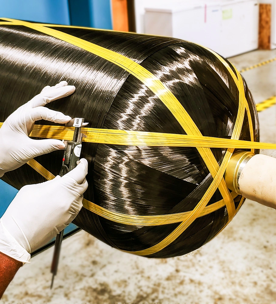 Gloved hands measuring the yellow reinforcement on a composite pressure vessel during manufacturing.