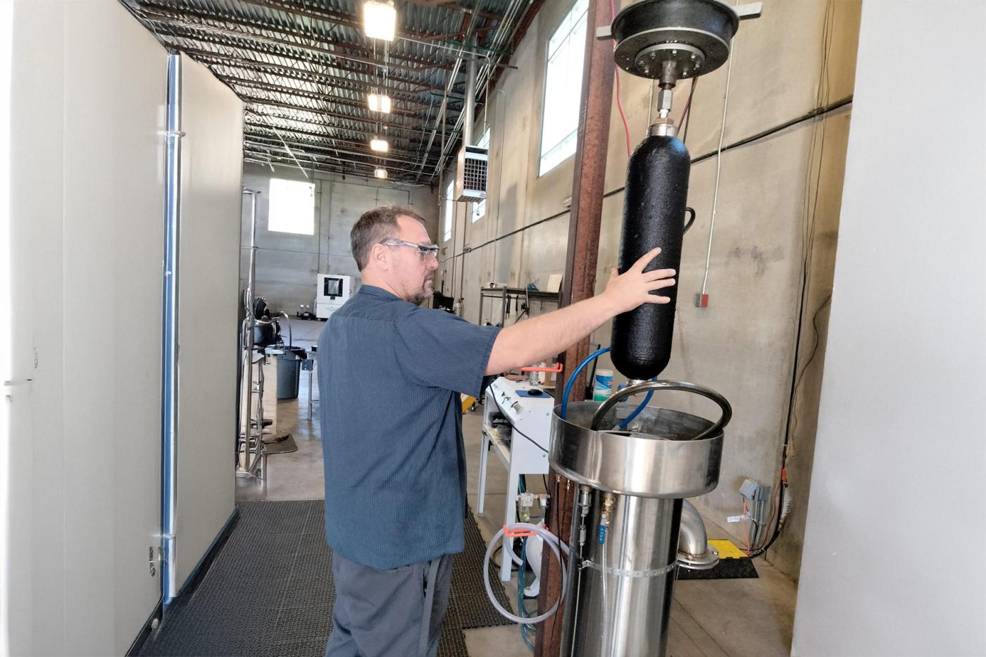 Technician loading a composite pressure vessel into a water jacket proof chamber for hydrostatic testing during recertification.