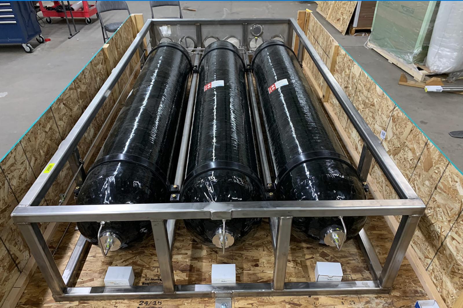 Close-up of 18 kg hydrogen storage tank with custom steel frame and strap mounting system for secure ground installation.