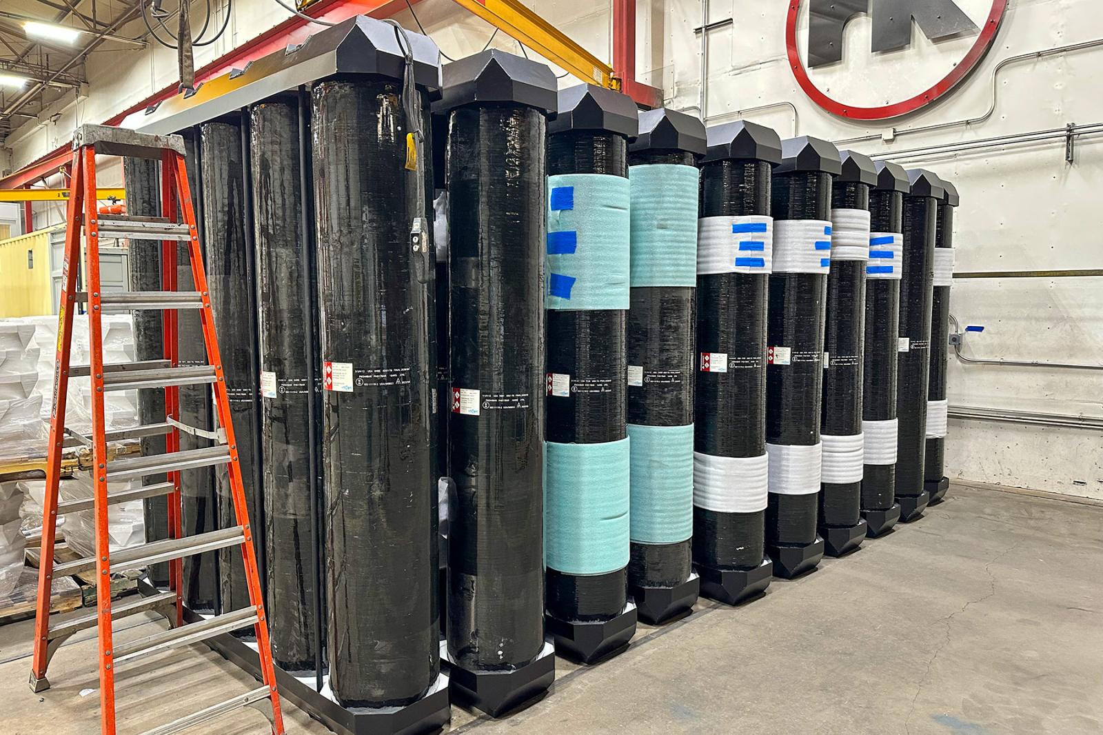 Composite overwrapped hydrogen pressure vessels (COPVs) arranged for installation in an ISO container, showing dome and neck mounts.