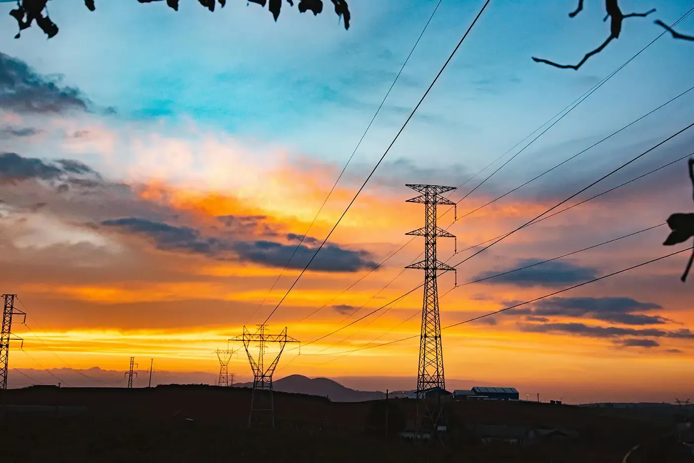 Silhouette of high-voltage electric transmission towers at sunset—symbolizing the transition to cleaner energy infrastructure, grid modernization, and hydrogen integration.